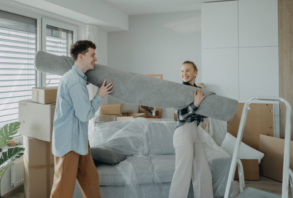 two persons holding a carpet into the room